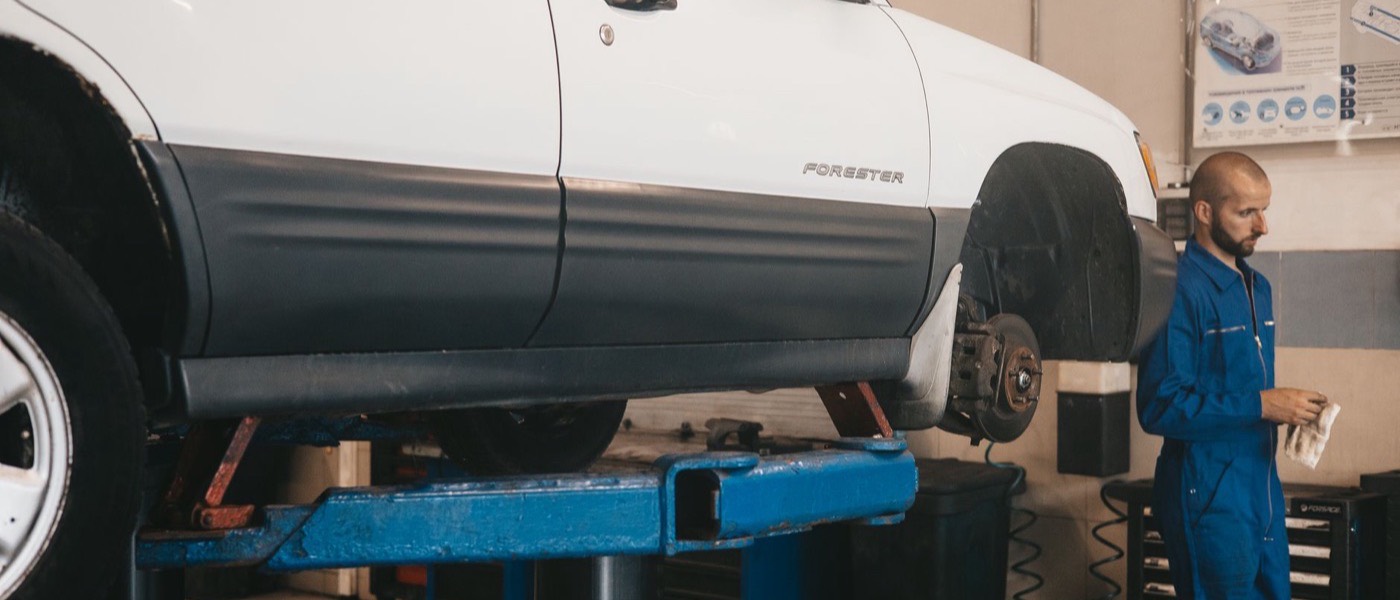 A mechanic working on a vehicle raised on a lift in a repair workshop.