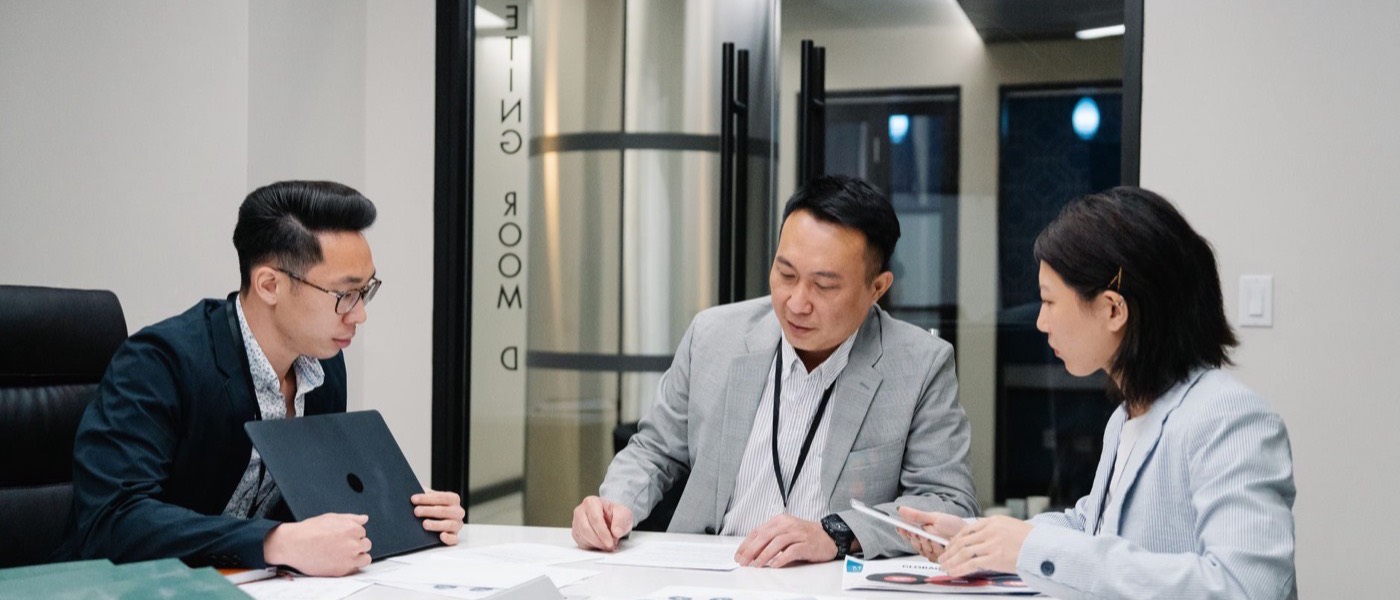Three colleagues reviewing documents together in a meeting room.