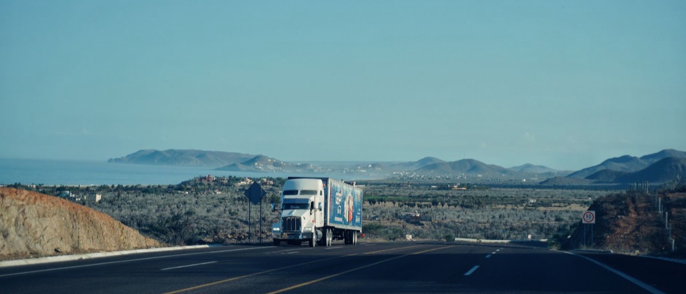A tractor-trailer travelling a highway through open country.